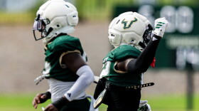 two football players pass each other running in different directions, both wearing dark green jerseys and white helmets 