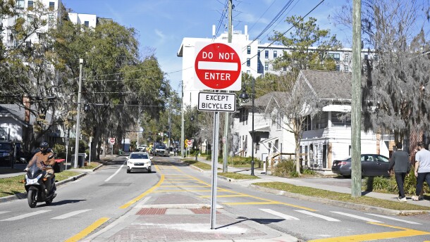 Pedestrians and a motorcyclist walk past one-way signage visible on Tuesday at the traffic circle at the intersection of Southwest Second Avenue and Southwest 12th Street in Gainesville.