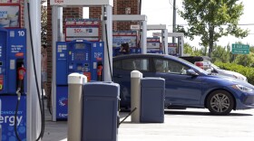 A medium shot of gas station pumps.  A blue sedan is parked at a pump. 