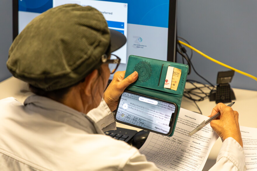 A woman uses a translator on her phone to fill out enrollment forms for NexStep Alliance.