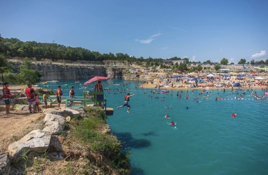  People in red flotation vests wait to cliff jump into the water. 