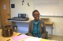 A woman smiles behind a desk covered in tax forms.