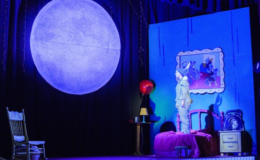 On stage: a person in pajamas stands on a bed and looks at the moon