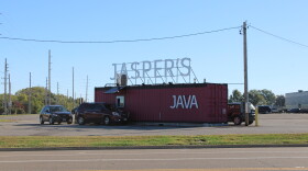 A shipping container converted into a double drive-thru coffee shop has at least three customers in line in their vehicles. 