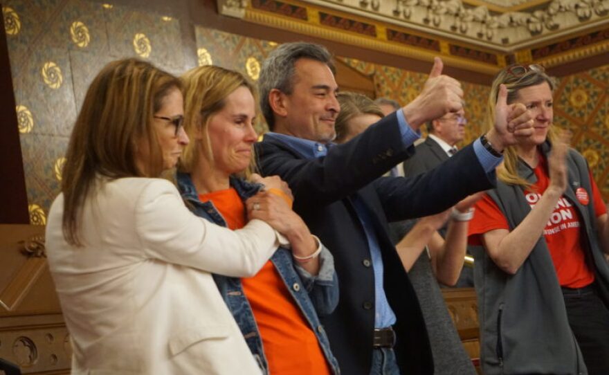 Ethan Song's parents, Kristin and Michael, gesture to lawmakers after passage of the bill they sought in their son's memory. Melissa Kane of Connecticut Against Gun Violence hugs Kristin.