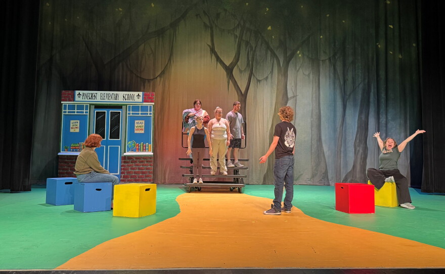 People standing on a green and yellow stage with red, blue and yellow blocks around the floor.