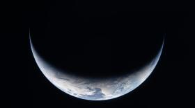 A sliver of Earth is illuminated against the blackness of space in this photo taken by an Artemis II crew member through an Orion spacecraft window on the third day of the mission.
