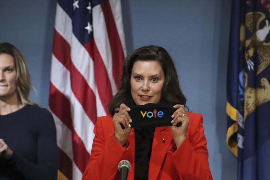 Gov. Gretchen Whitmer at a press conference holding a "vote" sign