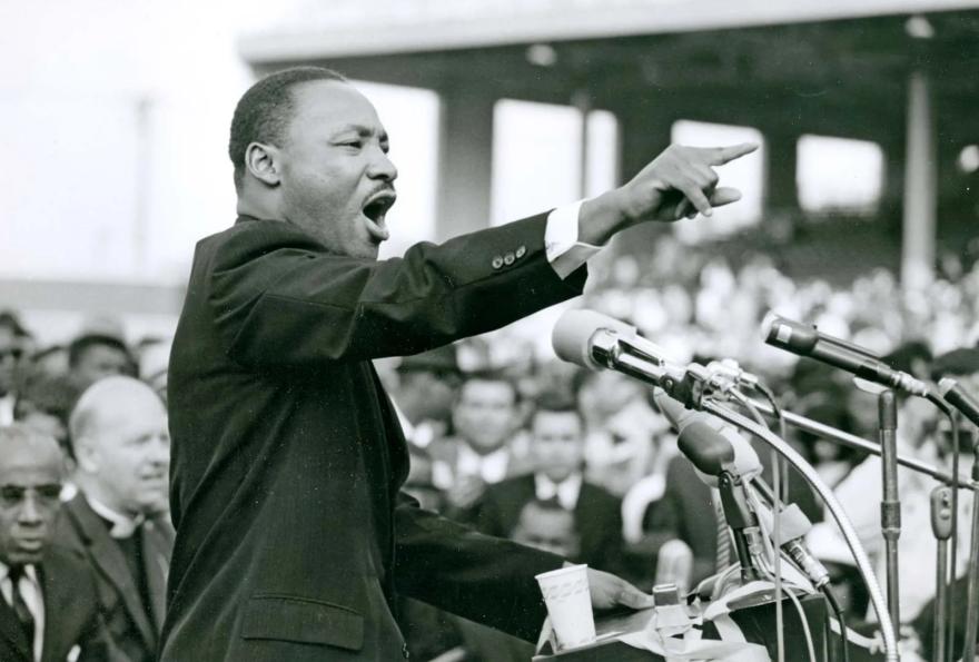 Black and white photo of a man speaking in front of microphones to a crowd