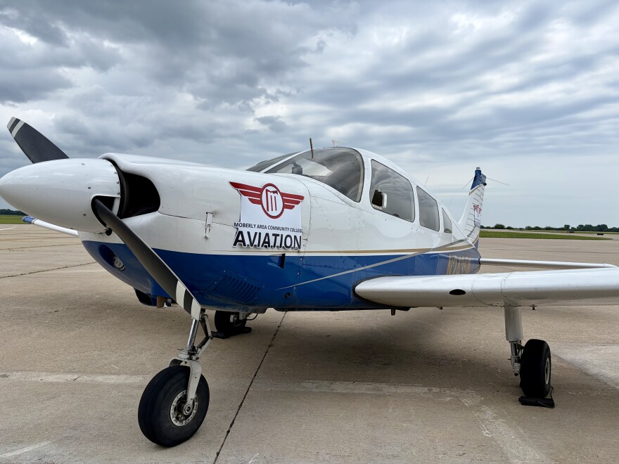A small 4-passenger blue and white aircraft is parked. There is a magnet logo on the side that reads "Moberly Community College Aviation."