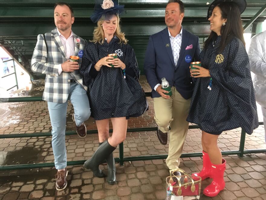 Sue Burke and Jason and Sarah Rodriguez take refuge from the rain under a staircase. Sue and Sarah ordered matching monogrammed ponchos six months in advance.