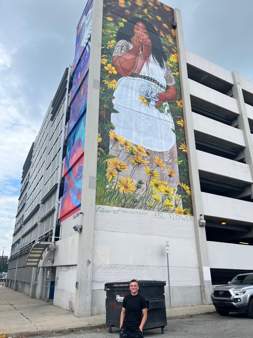 Mural Mania curator Alex Allen poses in front of the mural she says is her favorite this year. "Flower" by Richmond, Va.-based artist Nico Cathcorn, is an 80-foot-tall image of her friend using the American Sign Language word for "flower." Allen says she plans to ask the Guinness Book of World Records whether it's the world's largest image of someone using ASL.