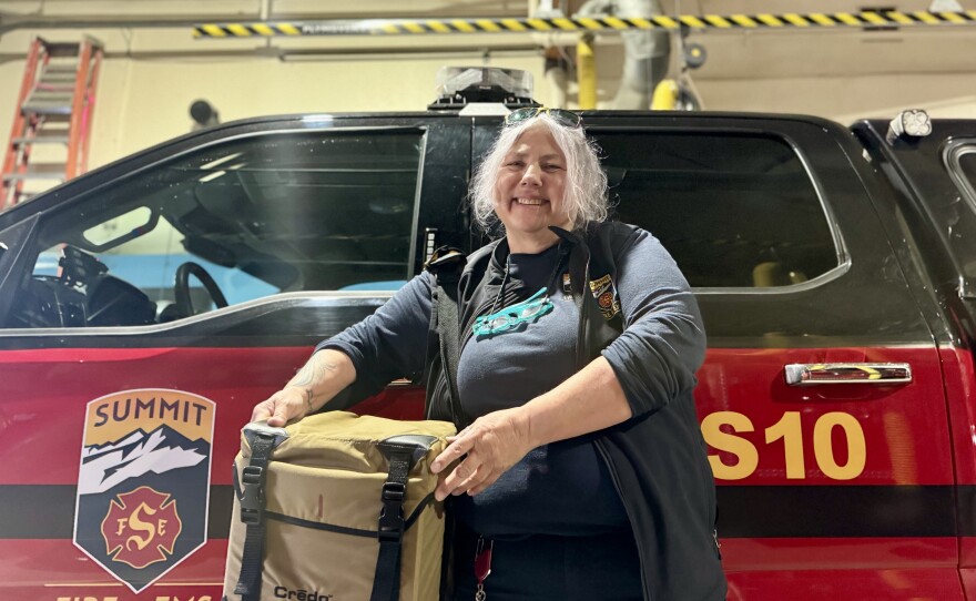 Jill Ridenhour holds a cooler in front of a pickup truck in a fire station.
