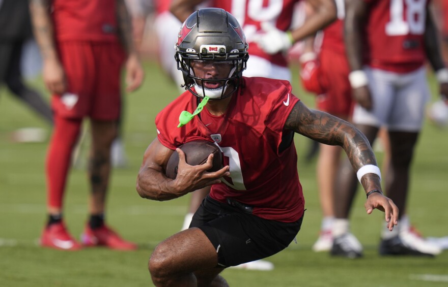 football player in red jersey and pewter helmet carries the football while running and looking ahead 