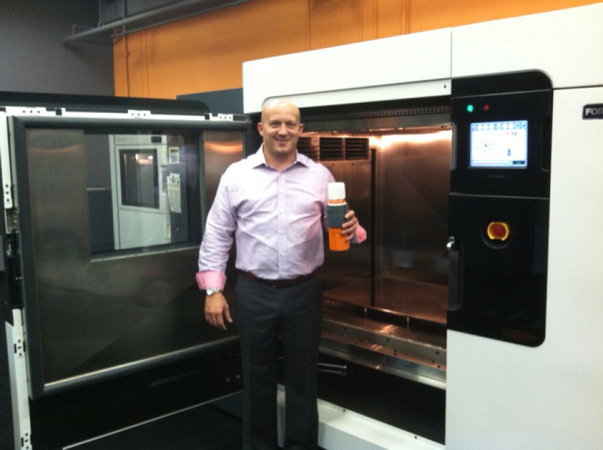 Matt Hlavin stands in front of a rapid prototyping and manufacturing machine. These can produce small batches of plastic