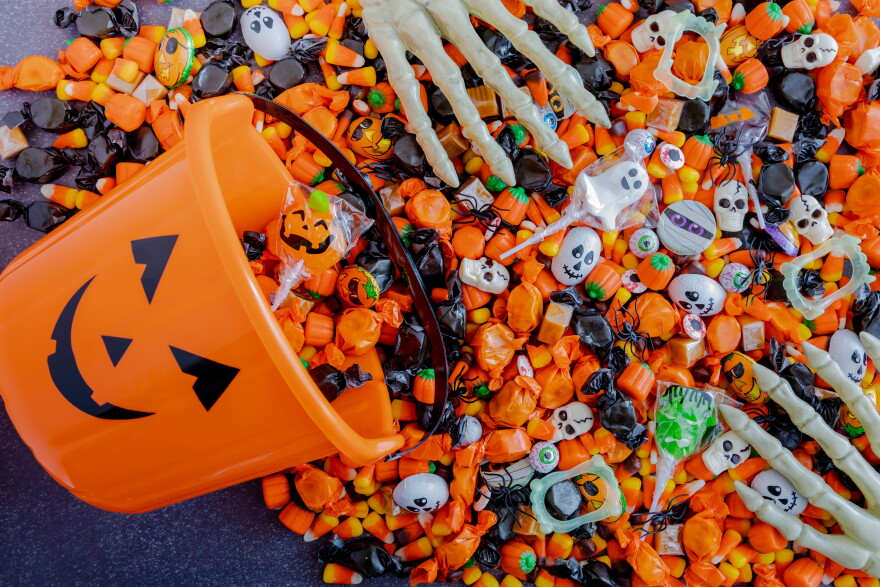 Orange pumpkin pail spilling Halloween candy on black stone surface with skeleton hands grabbing candy
