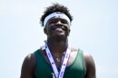 Martez Manuel grins, he has curly black hair, gold earrings, a white Nike headband. and is triumphantly wearing a medal around his neck alongside a gold necklace displaying an M with a crown.