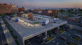 A computer design of the new facility in an aerial view with several buses and cars parked around the area.