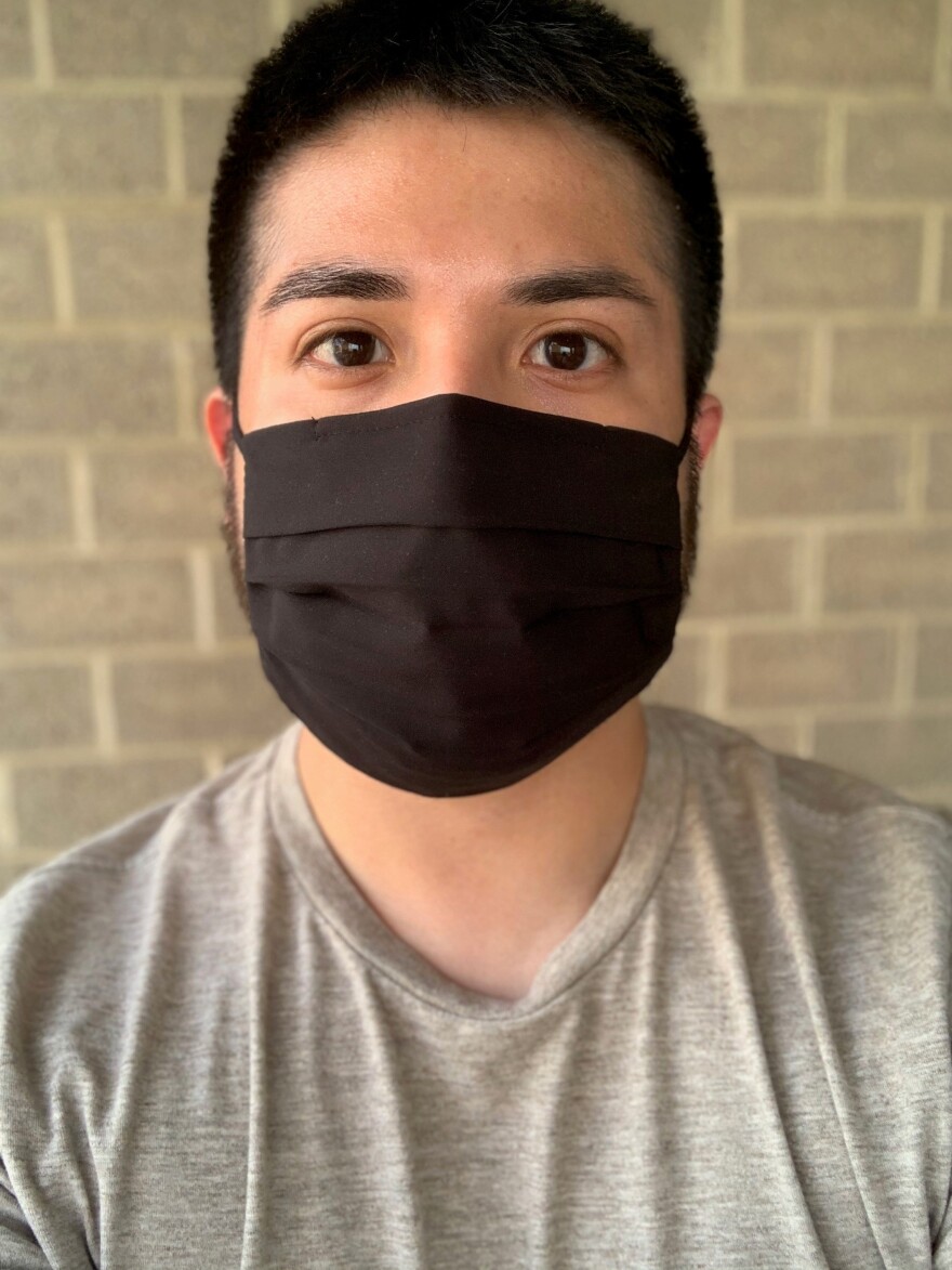 A man poses in a black face mask and gray shirt.