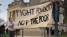 Rally members hold a sign reading "Fight Poverty, Not The Poor" on the courthouse steps.