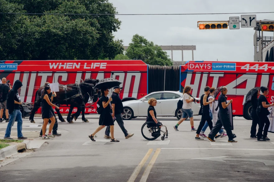 Protestors in funeral dress walk down Guadalupe Street alongside UT-Austin.