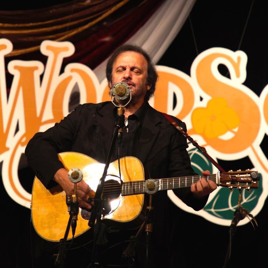 Michael Johnathon playing an acoustic guitar on stage at the Woodsongs Old Time Radio Hour.