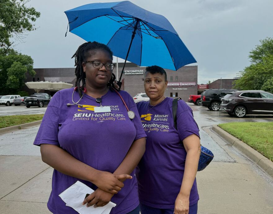 Monique Clark and Lisa Jones, both employees of Encompass Medical Group, stand outside in the rain picketing for higher wages.