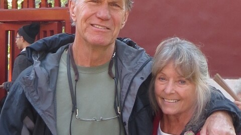 A man and woman stand together, the man has his arm around the woman. 