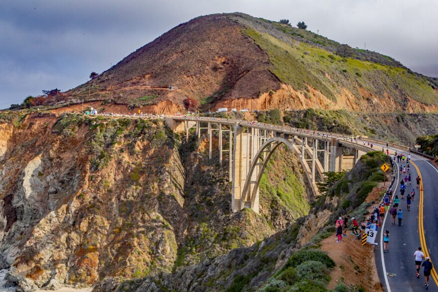 Highway 1 on the Big Sur cliffs during the 2022 Big Sur Marathon. Runners snake along one side of the highway.