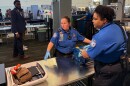 Two TSA officers in crisp blue uniforms scan luggage and carry-on items in Tampa International Airport. 
