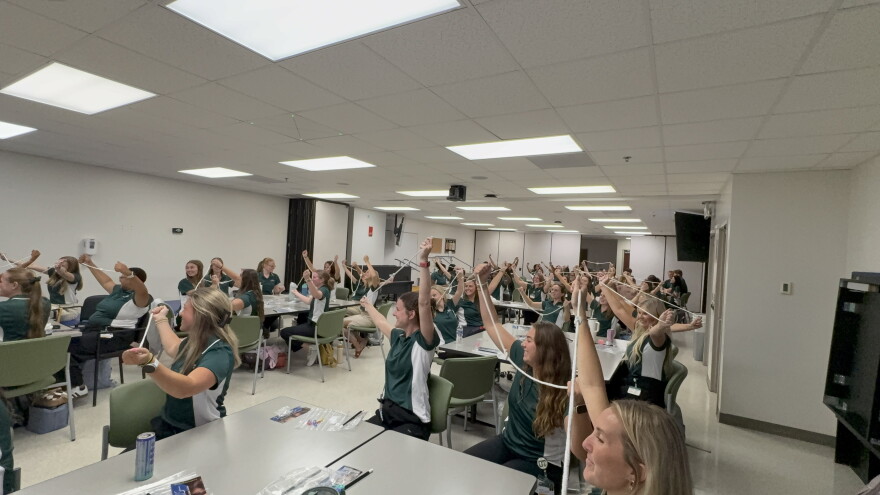 A classroom of college students sit in rows with each student holding a rope.