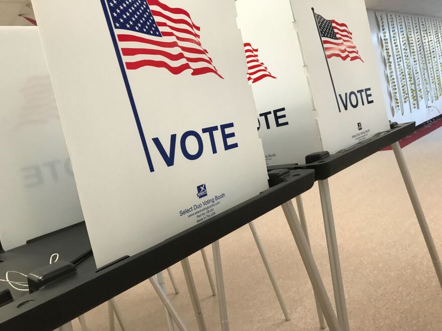 A row of voting booths. Each white tri-fold divider has the word "vote" and the American flag printed on it. 