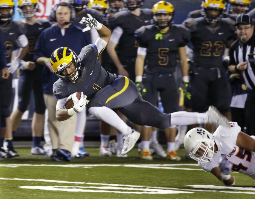 Bellevue running back Isaiah Gilchrist, left, leaps to avoid a tackle attempt by Eastside Catholic's Noah Failauga during the first half of the Class 3A high school football championship Friday, Dec. 4, 2015.