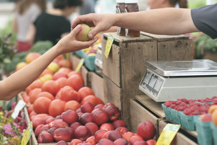 A person giving fruit to another at a market.
