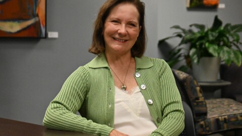 Woman looking at the camera and wearing a green sweater sitting at a table in an office setting.