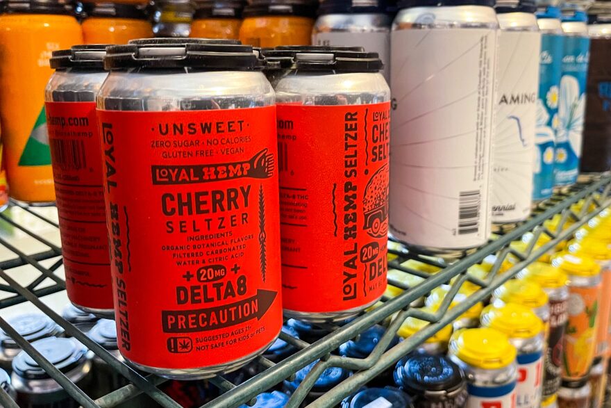 A four-pack of canned Delta-8 THC-infused cherry seltzers sit on the shelves of a store next to beer cans. 