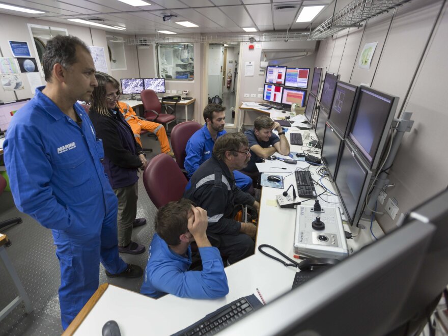 Dr. Tim O'Hara (far right) and a group of scientists crowd around a screen to see what a video camera lowered down into the abyss will show.