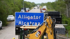 FILE - A loader holds a sign reading "Alligator Alcatraz" in its bucket as workers install it at the entrance to a new migrant detention facility at Dade-Collier Training and Transition facility, July 3, 2025, in Ochopee, Fla. (AP Photo/Rebecca Blackwell)