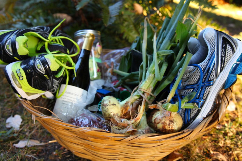 A basket given away to the Buy Nothing community that includes two pairs of running shoes, some fresh vegetables and a bottle of wine among other items.