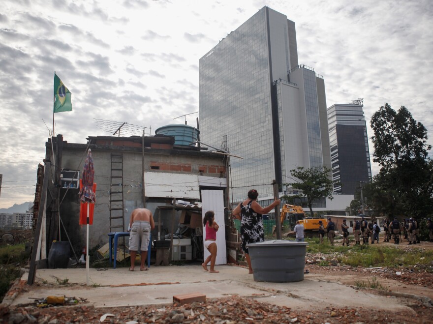 With the Olympics just months away, many wonder whether hosting the Games will be worth the effort. Here, members of the Lopes family watch during the demolition of a building in Rio's Vila Autodromo favela, with new Olympic Park structures in the background, on Feb. 24.