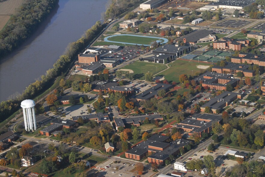 An aerial view of the Vincennes University campus in the fall, showing a large water tower, several brick buildings, sports fields, and a river running along the left side of the campus. 