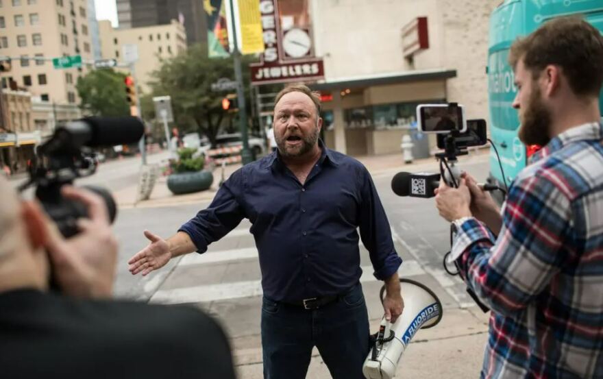 Texas conspiracy theorist Alex Jones records a video for his Infowars show on a street corner in downtown Austin in 2018. While bankruptcy filings for three of his companies earlier this month may be part of his legal strategy to obstruct court proceedings in defamation cases that he has lost, they’re also the latest development in Jones’ downswing from his spot at the top of far-right media.