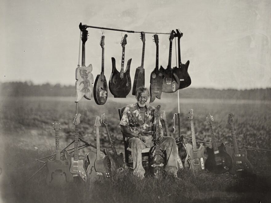 Luthier Freeman Vines sits with his hand-carved guitars in the tobacco field by his house, 2015.