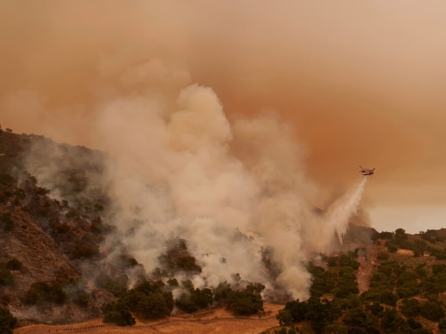 A water-dropping helicopter drops on flames from the advancing Lake Fire in Los Olivos, Calif., Saturday, July 6, 2024.