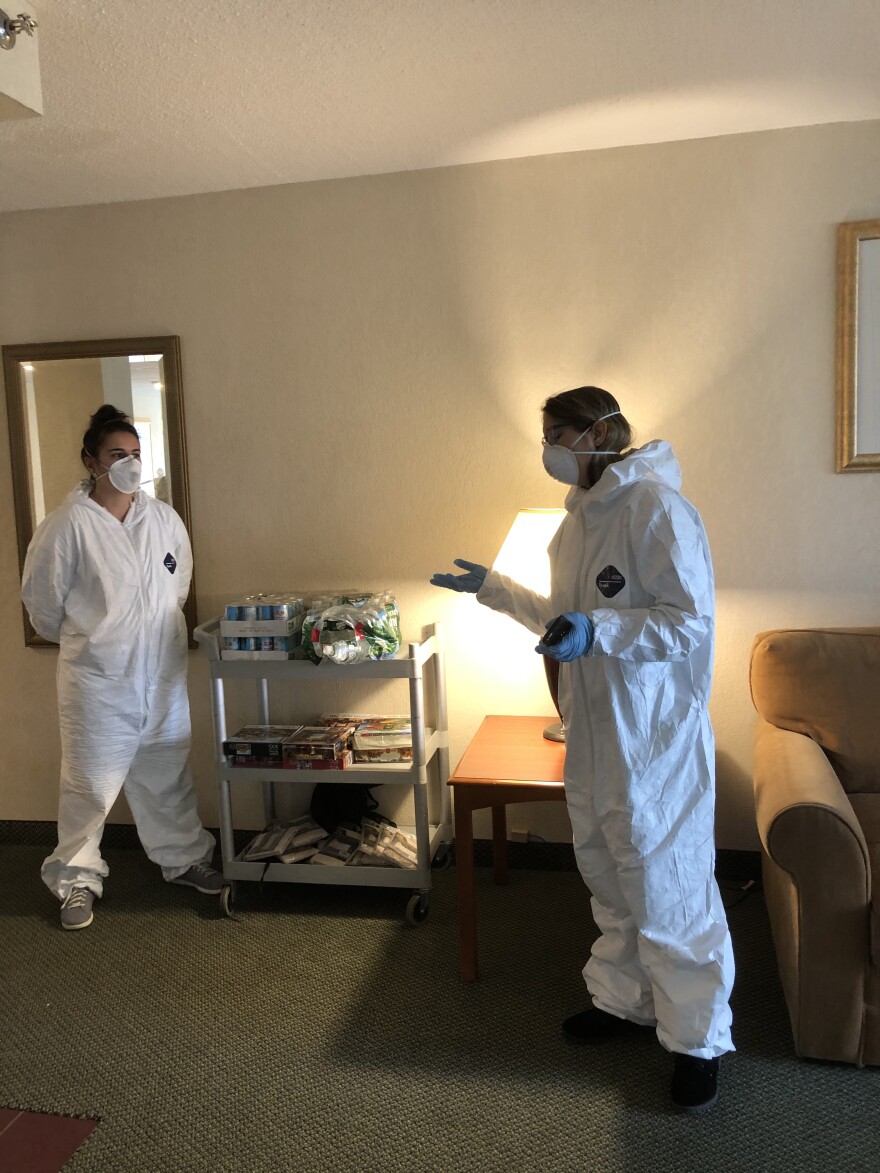 Two people in masks and protective suits talk.