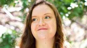 Headshot of Carly Sauvageau. She is standing outside in front of foliage and looking away from the camera while smiling.