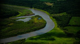 A river curves around bright green flood plains, forests and crop land.