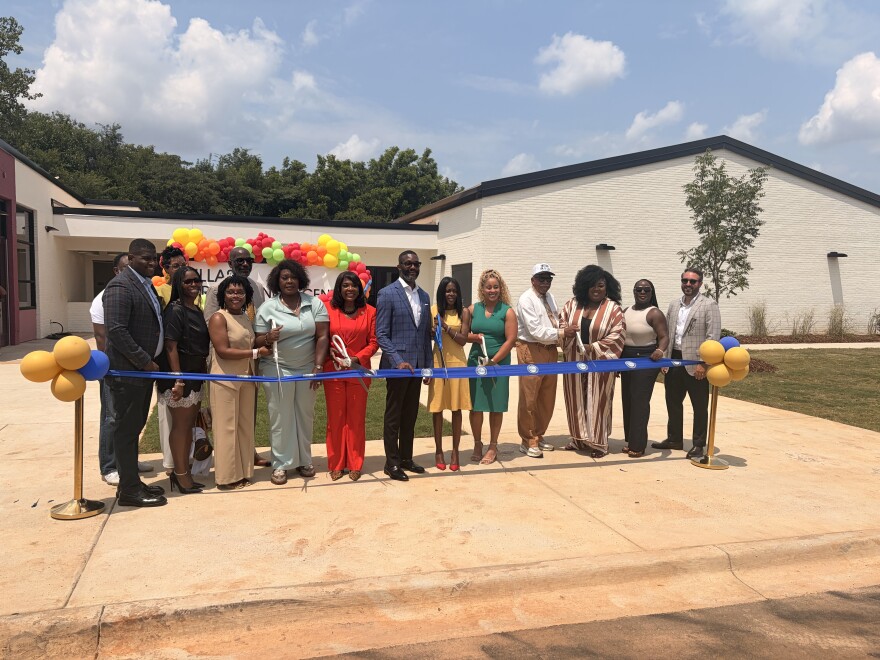 State, local and federal leaders stand behind a blue ribbon, ready to cut it marking the opening of a new early learning center in Birmingham's Titusville community.