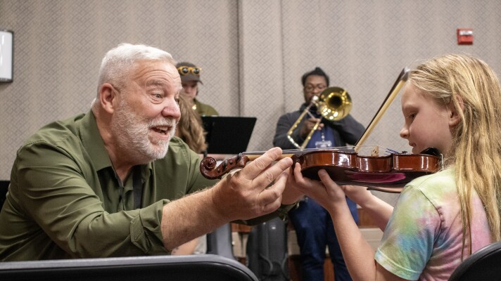 Steve, a Music & Arts instructor, corrects the placement of a violin during a mini-lesson at MCC's Homeschool Resource Fair.