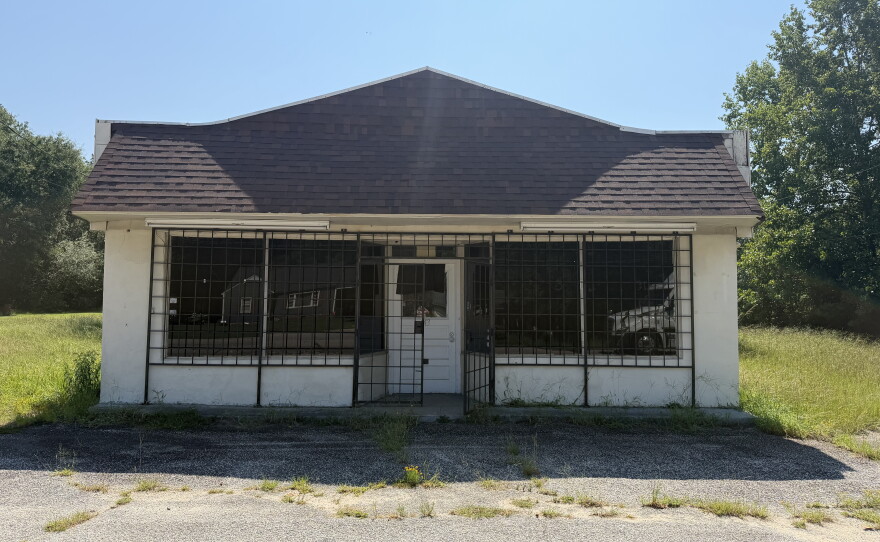 A small white house with a black shingle roof. There are black metal bars covering the windows and forming a gate in front of the door. 